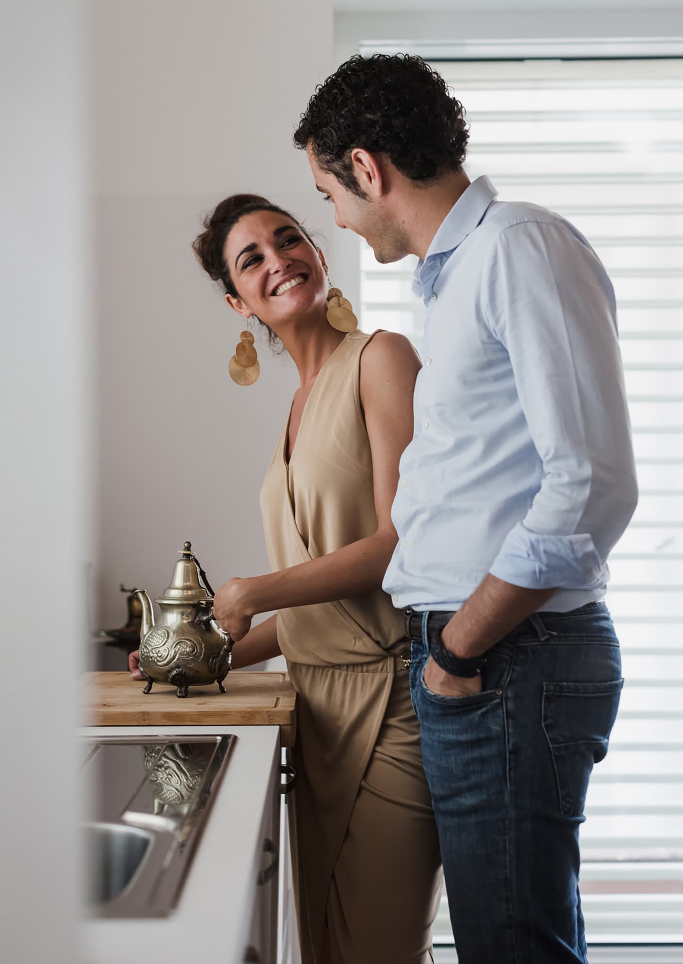 A man and woman smile at each other while preparing coffee in a luxurious modern kitchen.